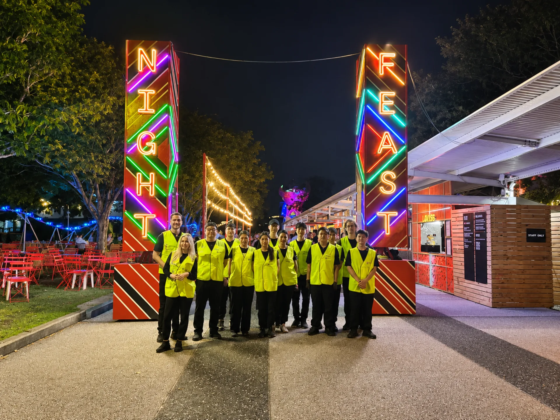 A large New Era event crew in high-visibility vests assembled at the entrance of a night food festival